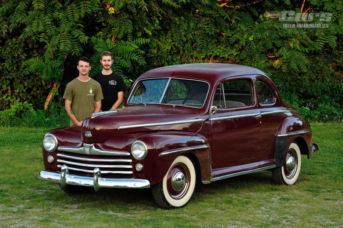 متطوعو ناتمس الشباب جون ماكولو وسكوت أرمسترونج مع سيارة فورد عام 1948 قبل تحول السيارة في مرآب ناتمس للسباق الكبير لعام 2022.