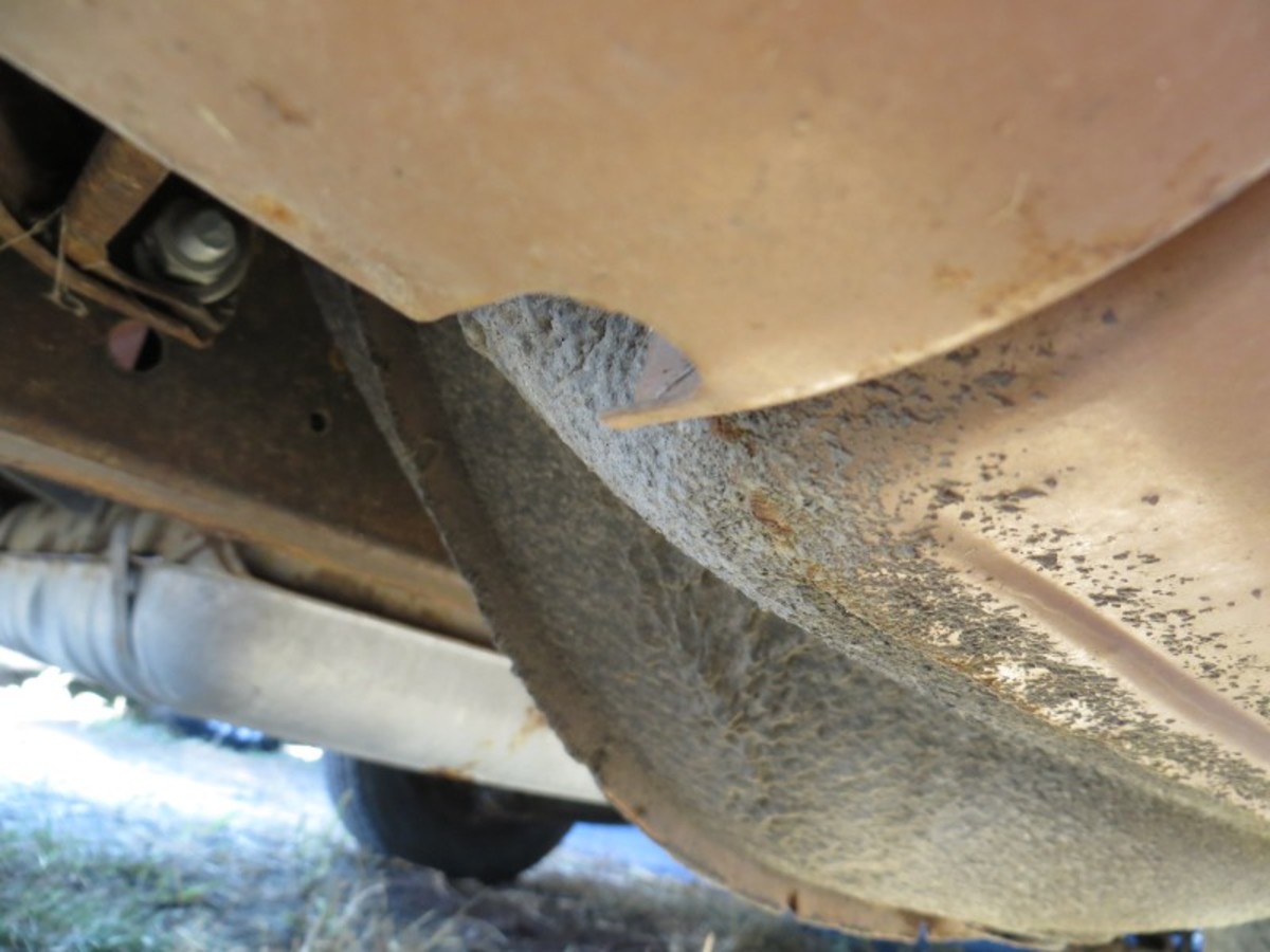 A view from the passenger rear shows overspray of sound deadening material from the spare tire well onto the bottom of the rear quarter panel and valence. 