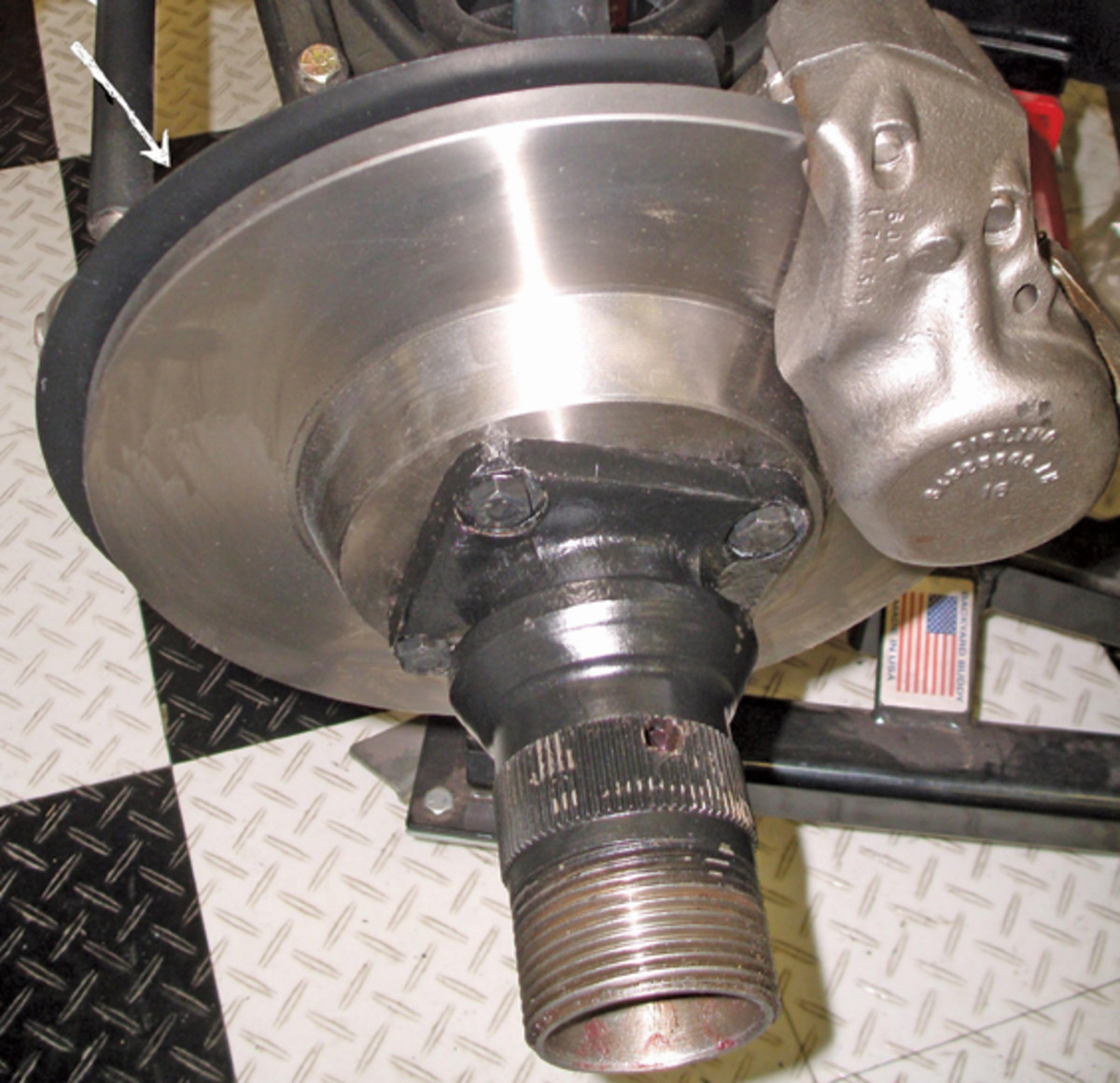 A stainless sleeved caliper rebuilt by Brake & Equipment Warehouse mounts to two holes in front suspension member. The caliper mounting bolts are also used to hold the “backing plate” the arrow is pointing to, plus required shims.