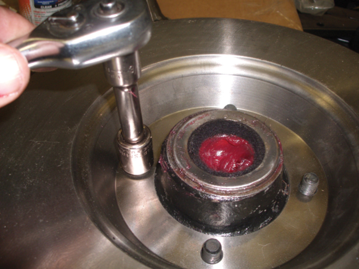 The inner end of the hub passes through the new brake rotor and bolts in place. Grease is added to fill the void between inner and outer bearings. Then, the felt seal is placed in the dust cover, which is tapped into the outer end of the hub.