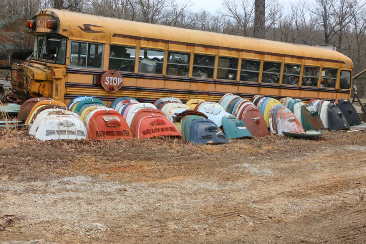A school bus is loaded with many good, small parts. Stacked alongside are rear engine covers that have been removed and are ready to ship.