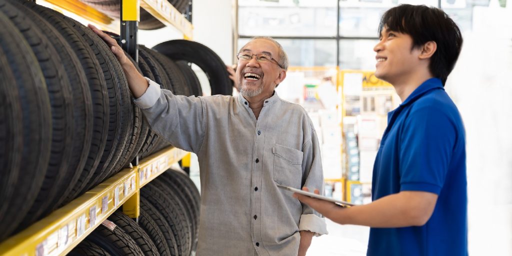 Car service. Asian salesman recommend new tire wheel on shelves shelf to senior elderly customer at the auto car repair shop