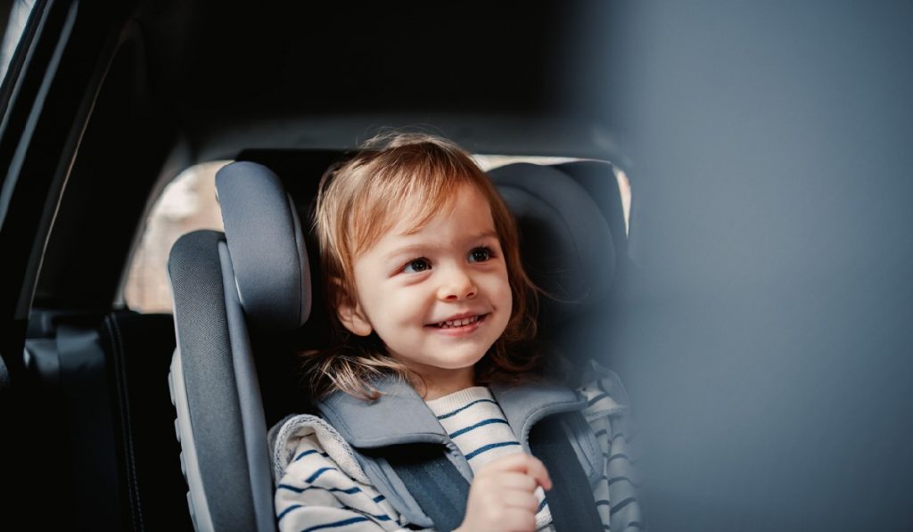 Happy girl having fun while sitting in car safety seat.