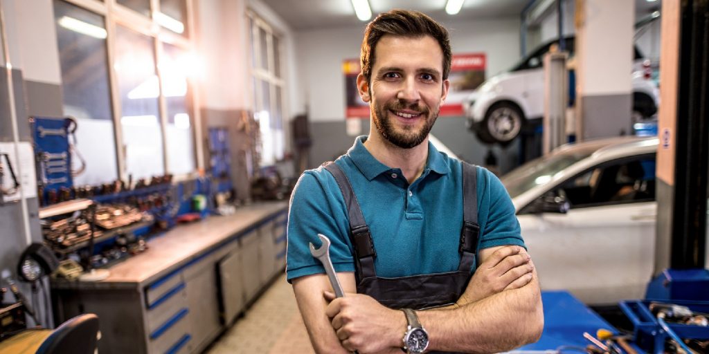 Young car mechanic working at car workshop and looking at camera.