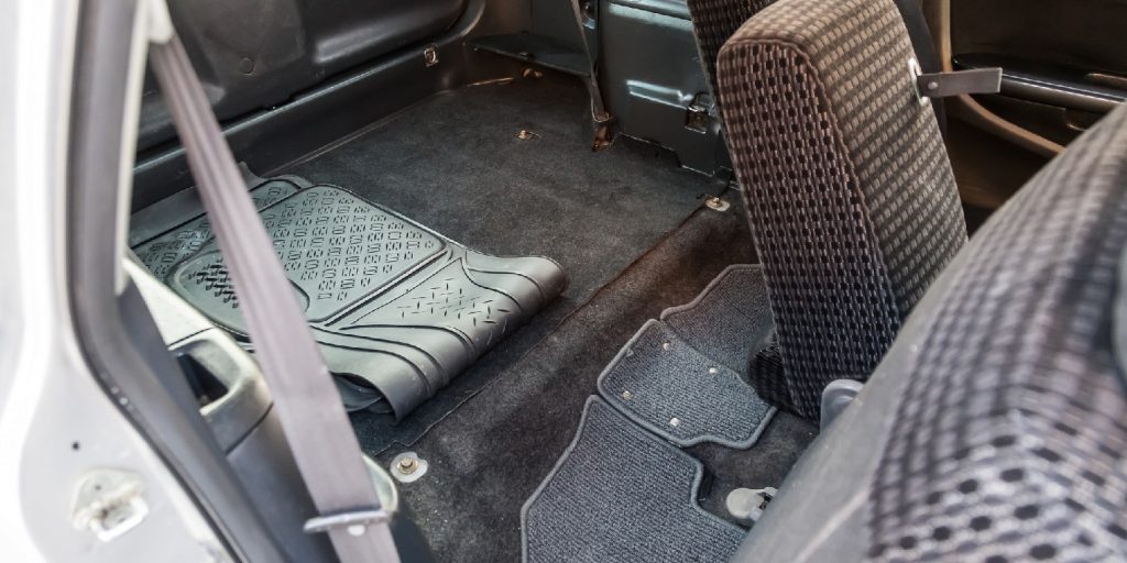 A view through the rear passenger seats inside the cabin of a Japanese station wagon to the roomy trunk with a black rubber mat after dry cleaning.