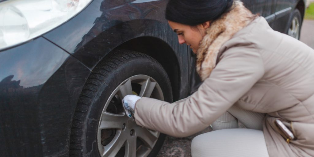 Beautiful young woman tightening bolts on her car tire while changing to winter tires