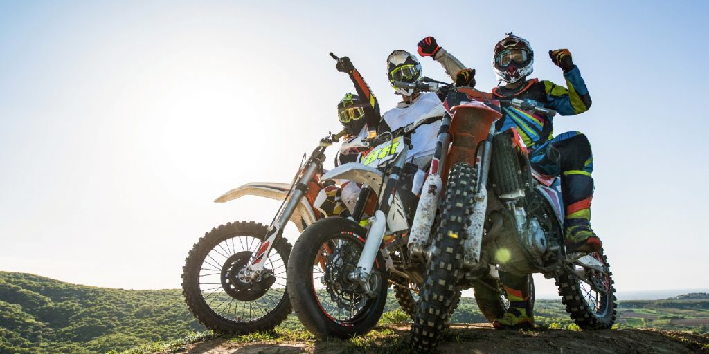 Low angle view of three motocross riders on stunt bikes on top of hill with hands raised.