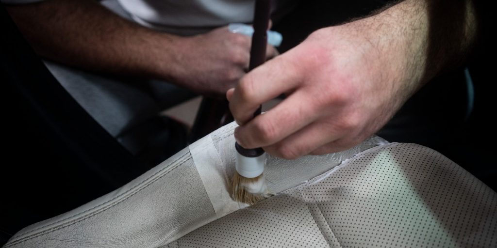Man cleaning leather car seat with fine brush