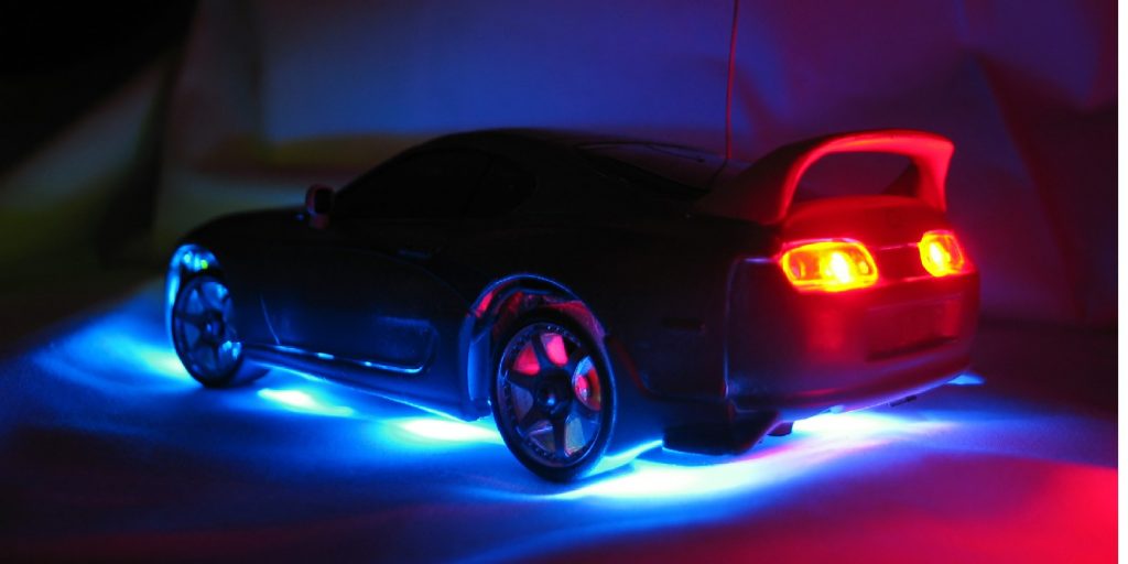 A macro shot of the rear of a remote control model street racer car in the dark with blue neon illumination under the body and red taillights.
