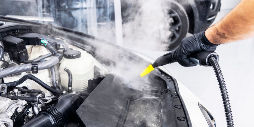 Car detailing. Car washing cleaning engine. Cleaning car using hot steam. Hot Steam engine washing. Soft lighting. Car wash man worker cleaning vehicle.