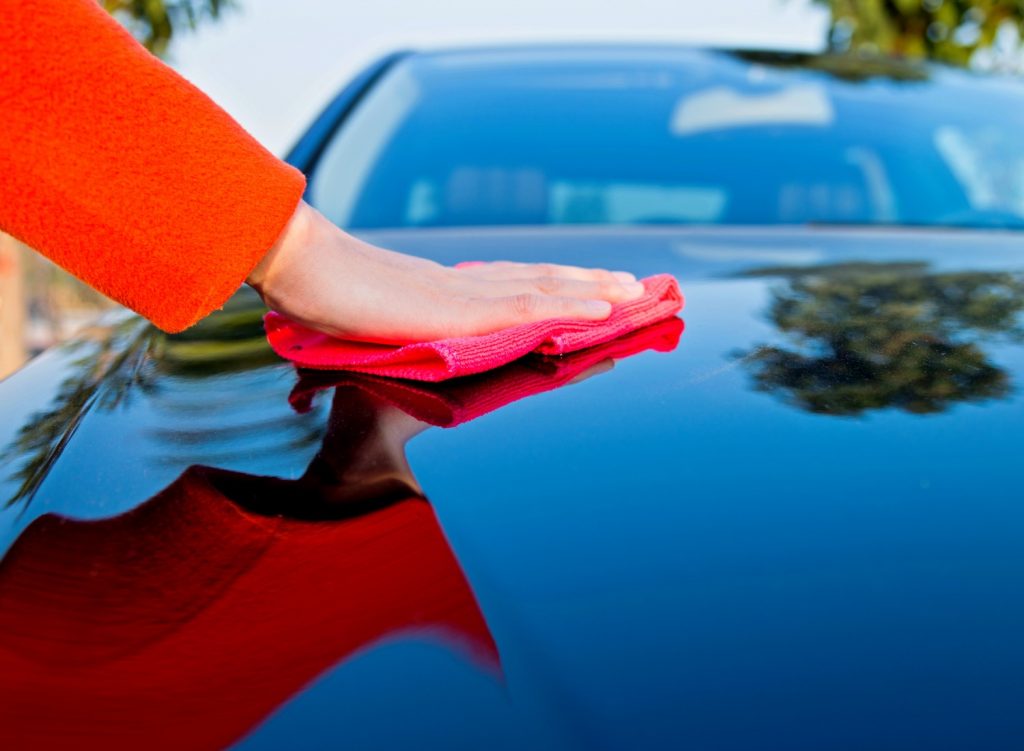 Person wiping a car hood with a cloth