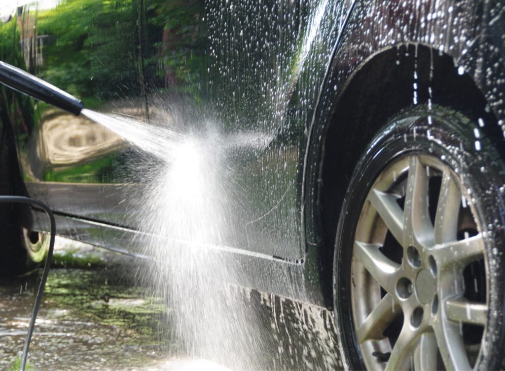 Person pressure washing a car