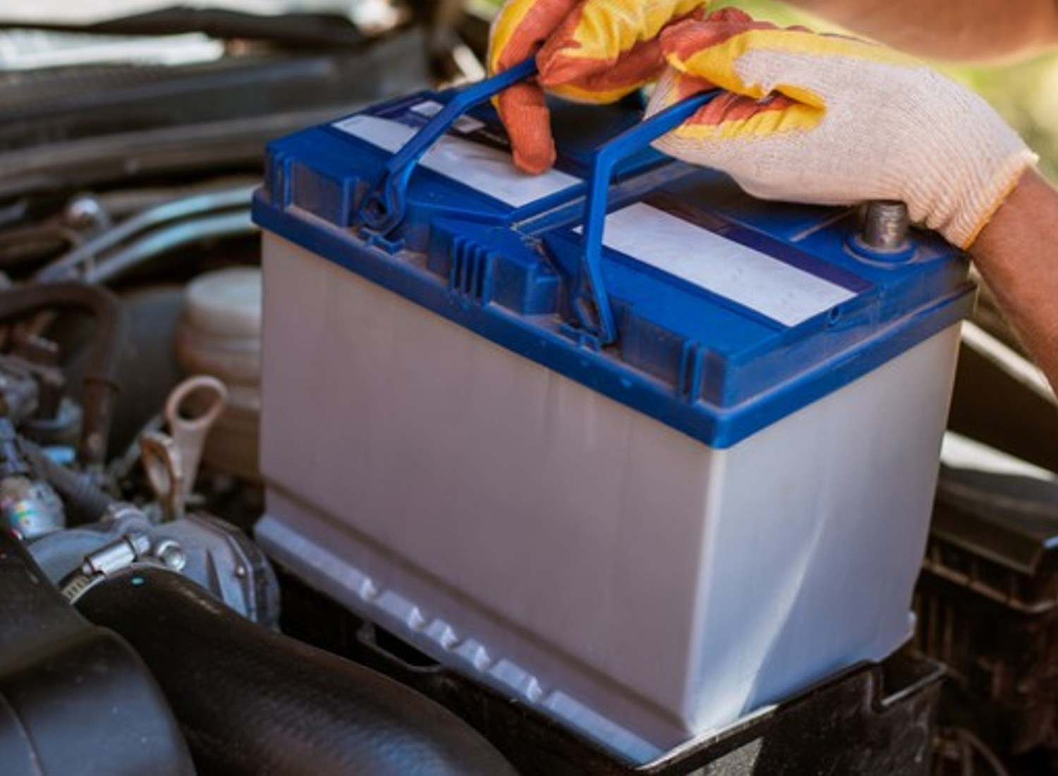 Image of someone wearing gloves placing a car battery into their car.